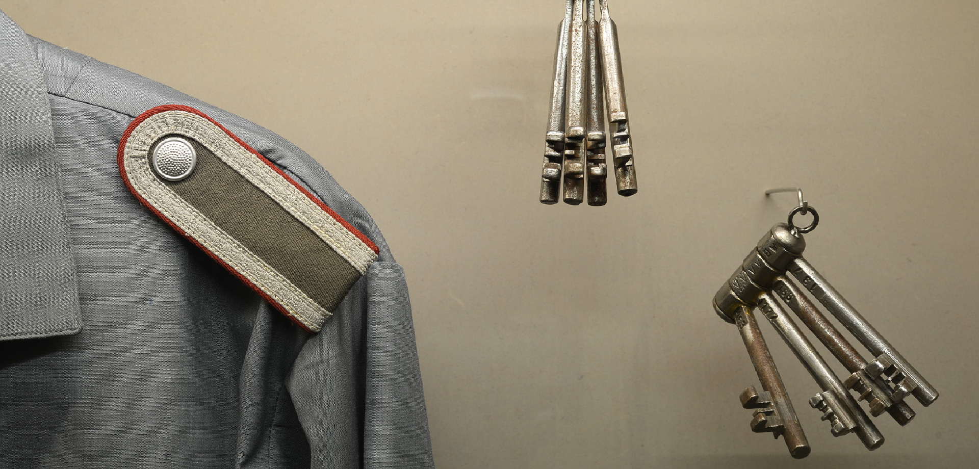 ein Teil eienr Uniformjacke mit Schulterholster, daneben hängen zwei Schlüssel