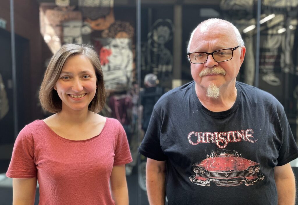 ein älterer Mann und eine junge Frau stehen nebeneinander, beide Lächeln in die Kamera