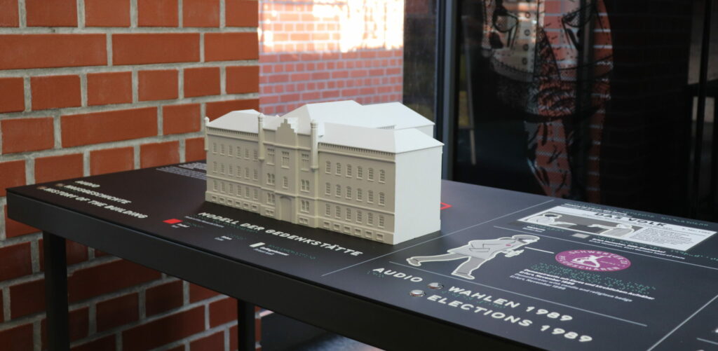 A table with a model of the building of the Memorial and Educational Centre. Drawings and texts on the table are also visible.