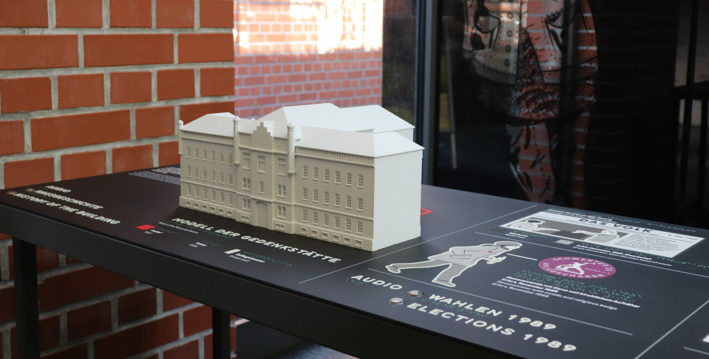 Ein Tisch mit einem Modell des Gebäudes der Gedenk- und Bildungsstätte. Ebenfalls auf dem Tisch zu sehen sind Zeichnungen und Texte.